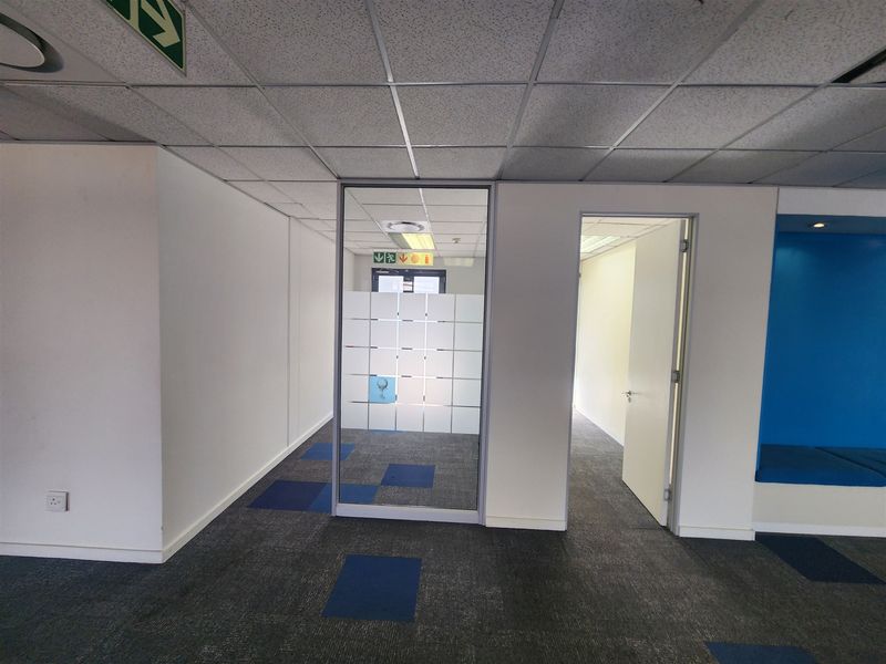 A vacant office space featuring carpet tiles, a suspended ceiling with recessed lighting, a glass partition, and a built-in blue bench seating area.