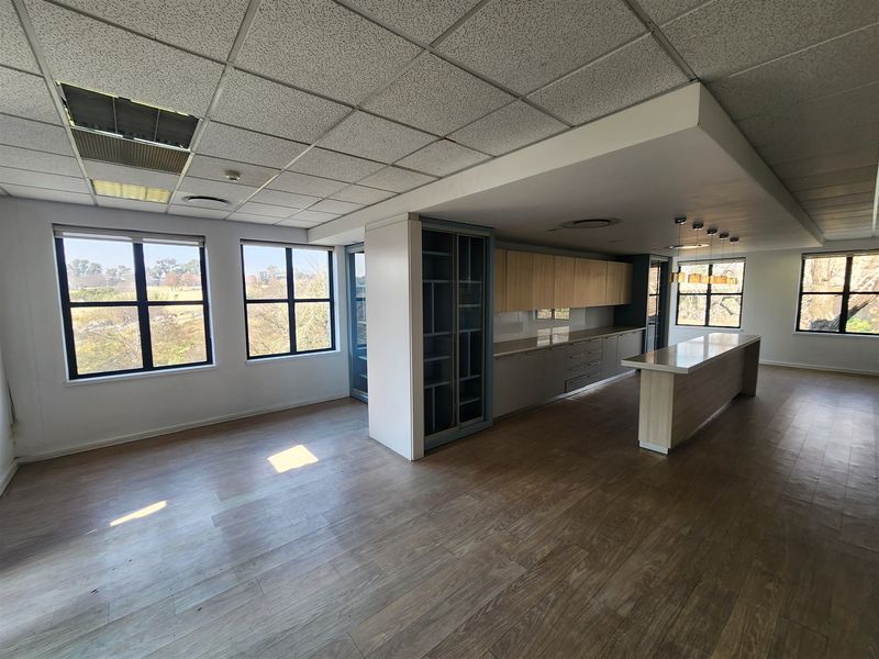 Spacious open-plan office area featuring laminate flooring, a modern kitchen island, built-in cabinetry, and large windows providing ample natural light.