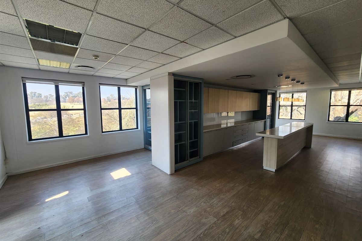 Spacious open-plan office area featuring laminate flooring, a modern kitchen island, built-in cabinetry, and large windows providing ample natural light.