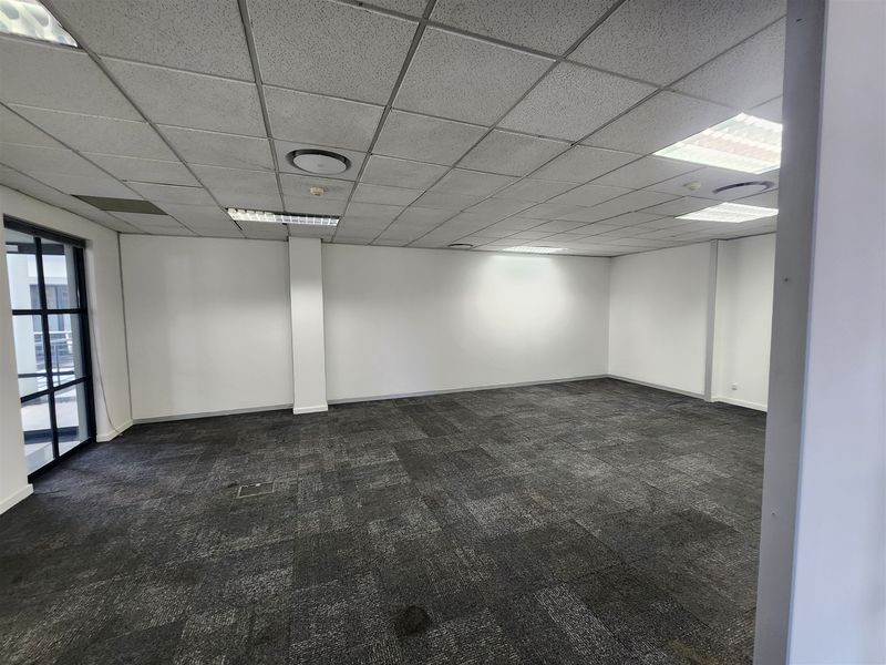 A spacious, empty office suite featuring neutral carpet tiles, a suspended ceiling with recessed lighting, and a large glass-paneled entrance door.