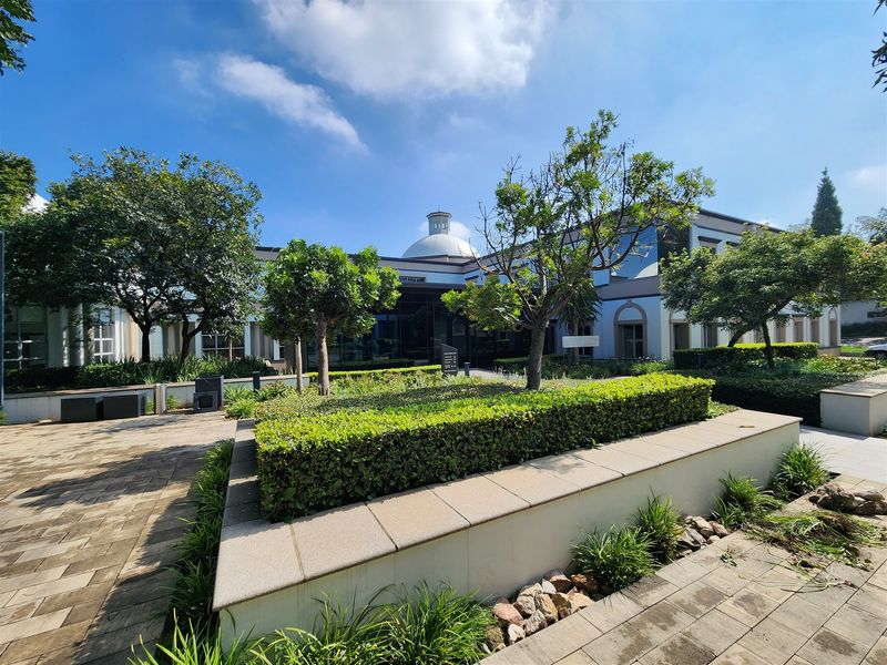 A well-maintained office building exterior featuring a landscaped garden, paved walkways, and a prominent central dome architectural feature.