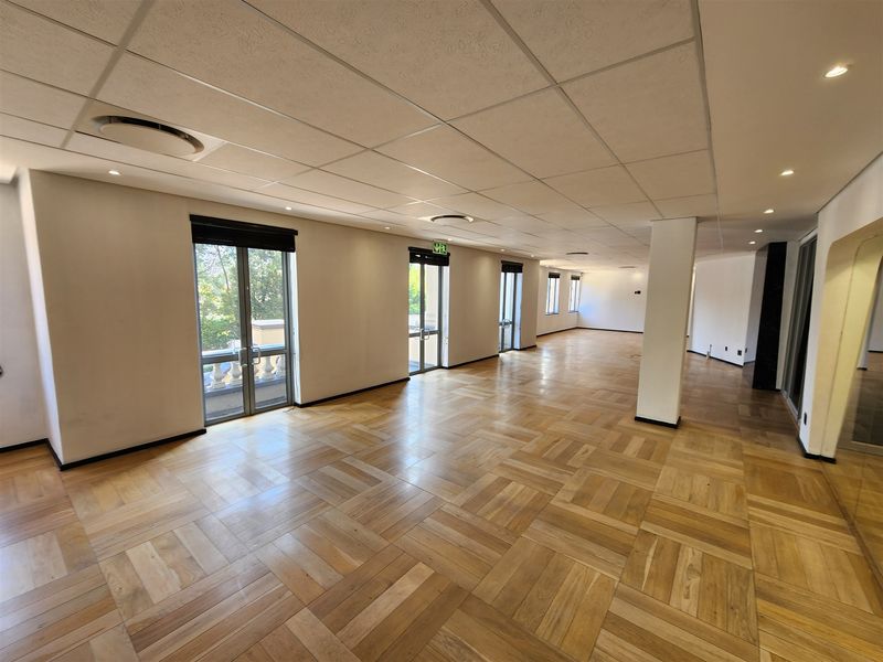 Spacious, open-plan office area featuring high-quality parquet flooring, a modern suspended ceiling with recessed lighting, and multiple glass doors providing natural light.