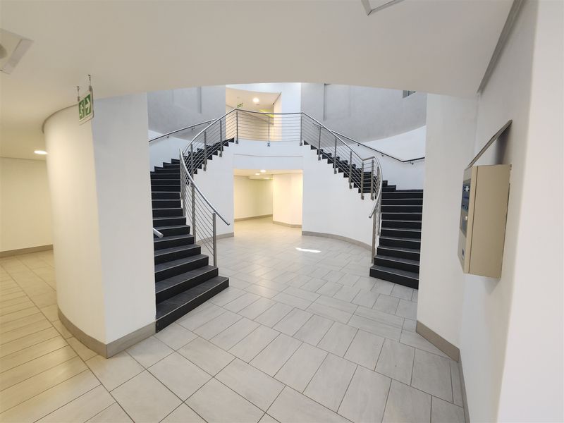 A modern office building entrance featuring a grand curved staircase with stainless steel balustrades and clean, neutral tiled flooring.