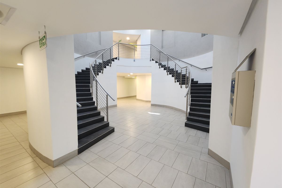 A modern office building entrance featuring a grand curved staircase with stainless steel balustrades and clean, neutral tiled flooring.