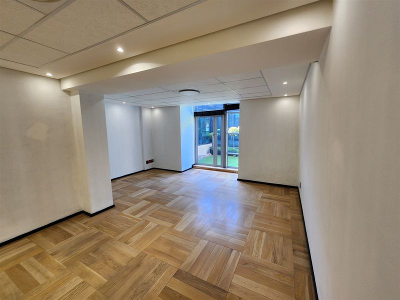 A bright, empty office space featuring parquet flooring, recessed lighting, and a glass sliding door leading to an outdoor area.