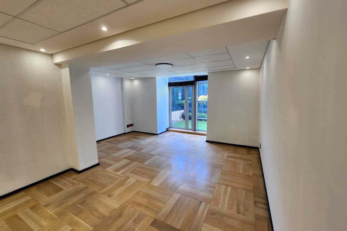 A bright, empty office space featuring parquet flooring, recessed lighting, and a glass sliding door leading to an outdoor area.