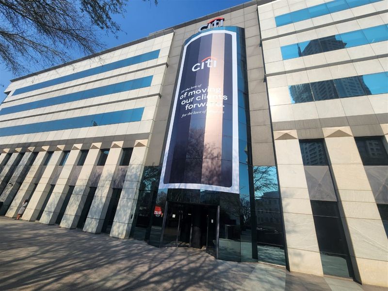 Front elevation of a modern multi-story office building featuring glass curtain walls, stone cladding, and prominent corporate branding.