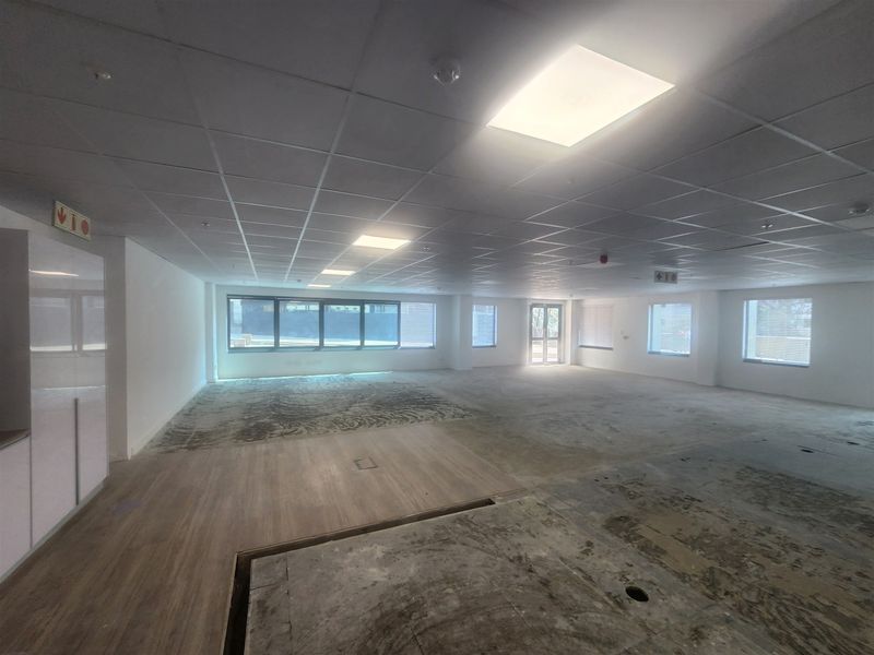 An expansive, open-plan office space featuring a suspended ceiling, recessed lighting, and large windows, currently awaiting final flooring installation.
