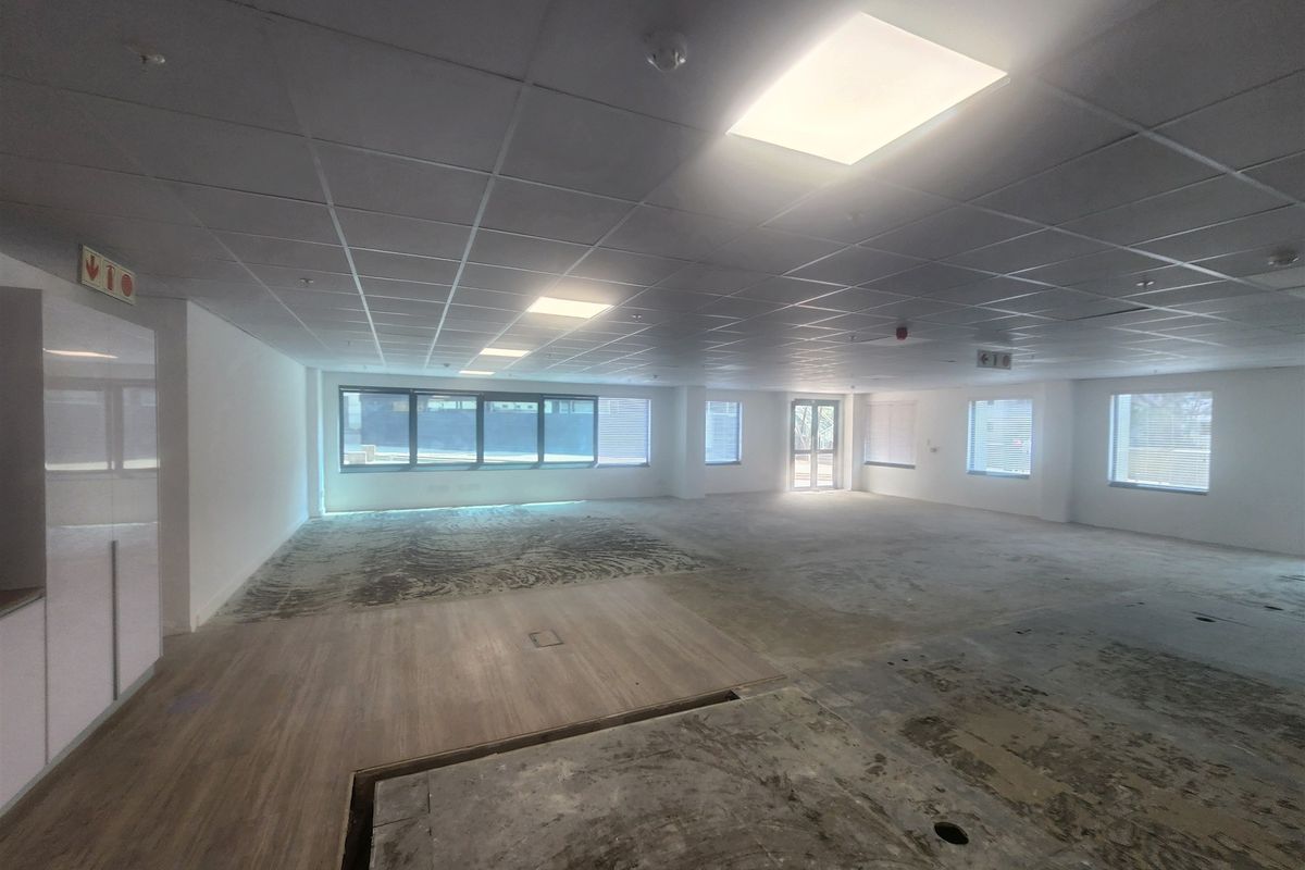 An expansive, open-plan office space featuring a suspended ceiling, recessed lighting, and large windows, currently awaiting final flooring installation.