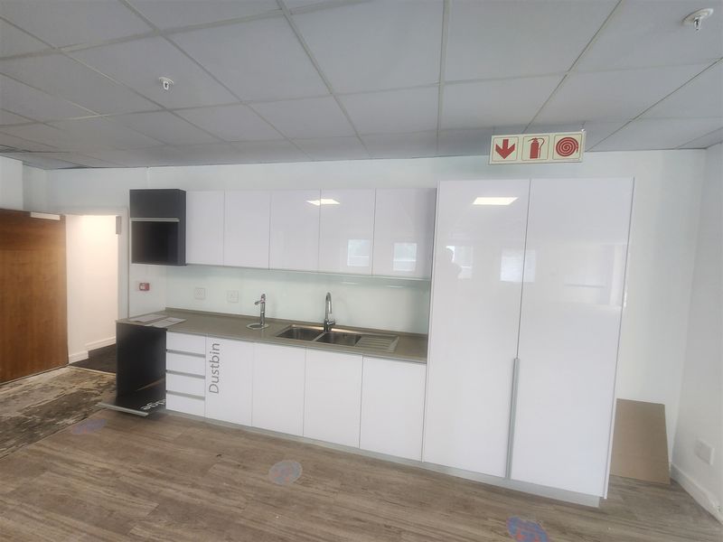 A clean, modern office kitchenette featuring white high-gloss cabinetry, stainless steel sink, and durable laminate flooring.