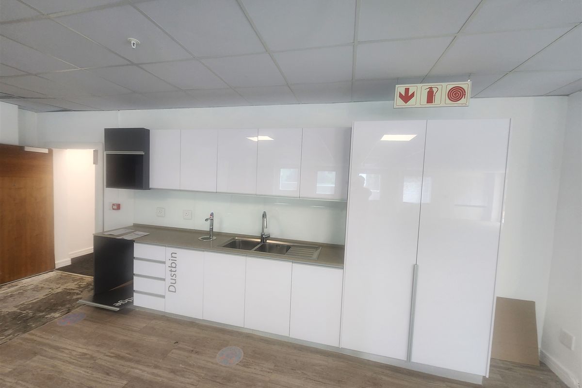 A clean, modern office kitchenette featuring white high-gloss cabinetry, stainless steel sink, and durable laminate flooring.
