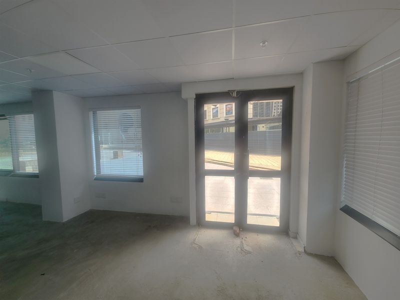 An empty office space featuring a suspended ceiling, concrete flooring, and double glass doors with natural light.
