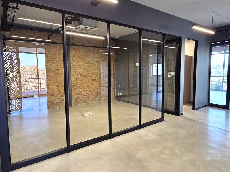 Modern open-plan office space featuring polished concrete floors, exposed brick accents, and sleek glass partitioning for a contemporary professional environment.
