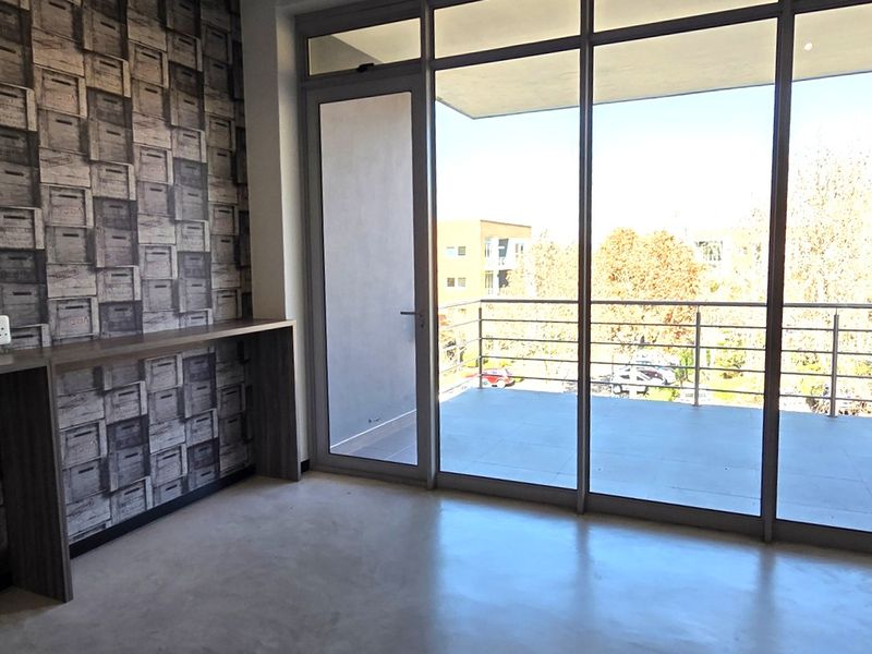 Modern office space featuring a built-in desk, kitchenette with sink, polished concrete flooring, and large glass doors leading to a private balcony.