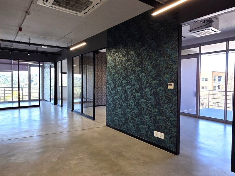 Modern open-plan office space featuring polished concrete floors, glass partitions, decorative feature walls, and integrated ducted air conditioning with ample natural light.