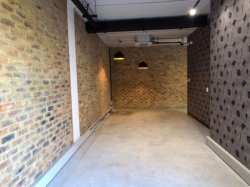 An empty office space featuring exposed brick walls, polished concrete floors, and industrial-style exposed ceiling services with pendant lighting.