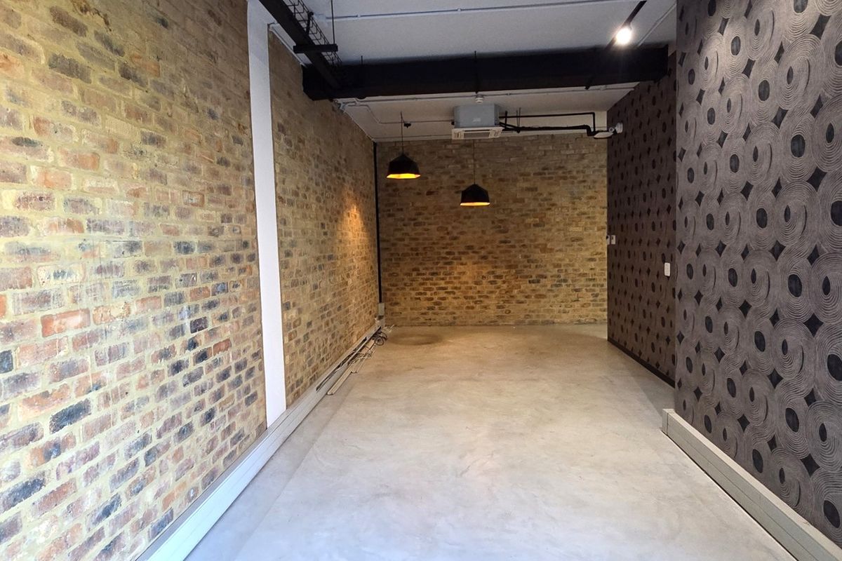 An empty office space featuring exposed brick walls, polished concrete floors, and industrial-style exposed ceiling services with pendant lighting.