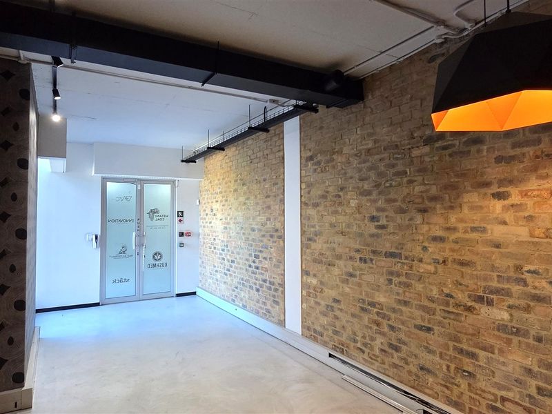 Modern office space featuring exposed brick walls, polished concrete flooring, and industrial-style exposed ceiling ducting with a glass entrance door.