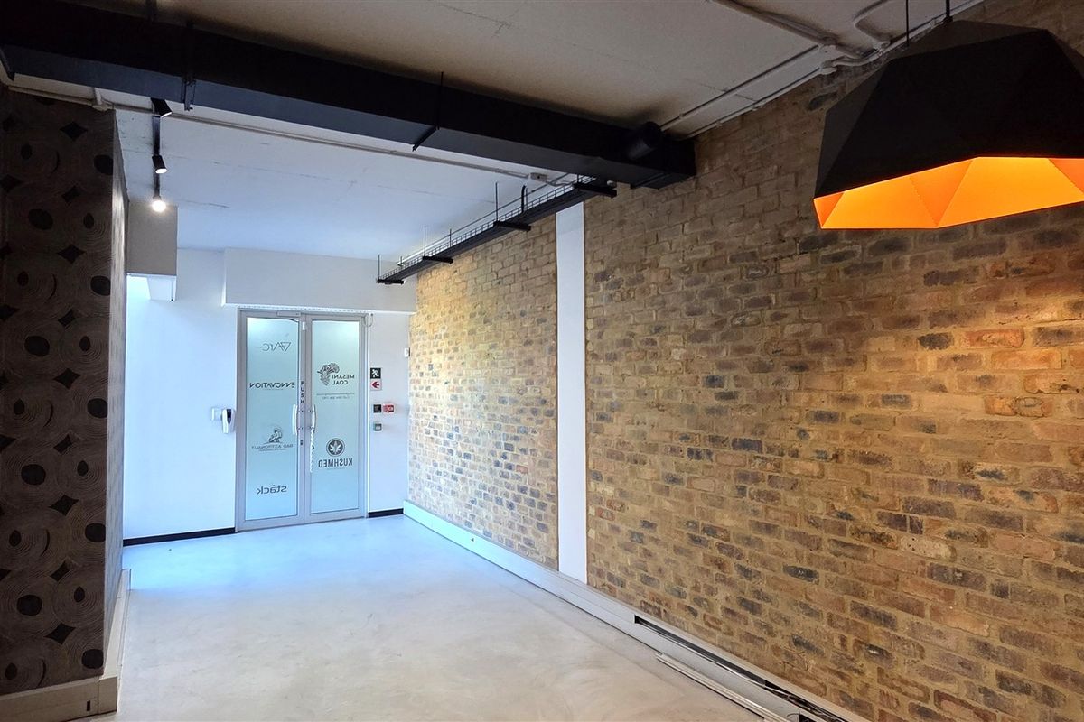 Modern office space featuring exposed brick walls, polished concrete flooring, and industrial-style exposed ceiling ducting with a glass entrance door.