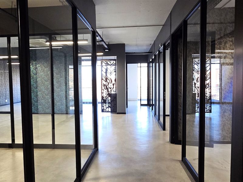 Modern office hallway featuring polished concrete floors, sleek black-framed glass partitions, and contemporary decorative metal screens, creating a professional and open workspace environment.