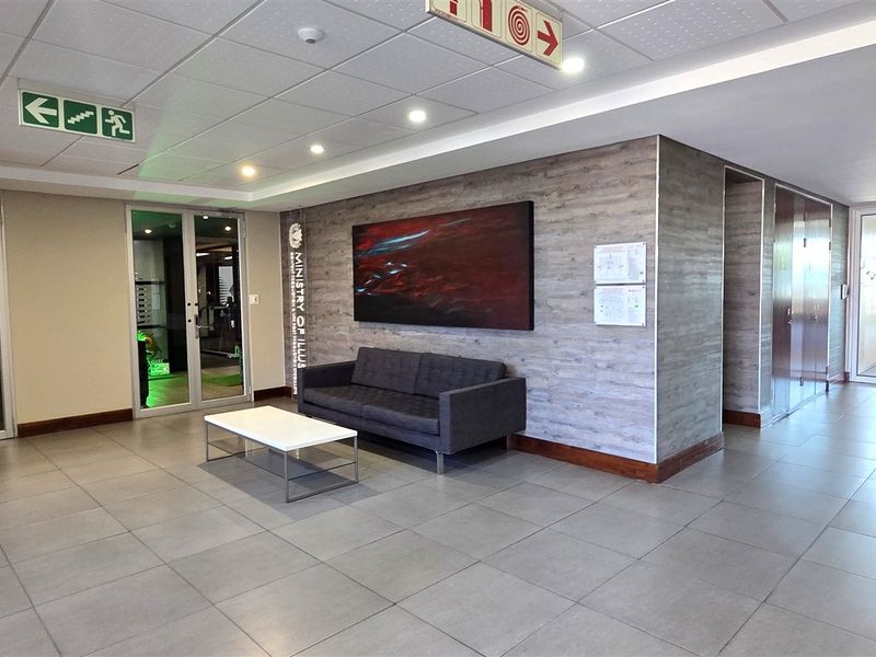 A modern office building entrance lobby featuring tiled flooring, a wood-look feature wall, recessed lighting, and multiple glass-panelled access doors.