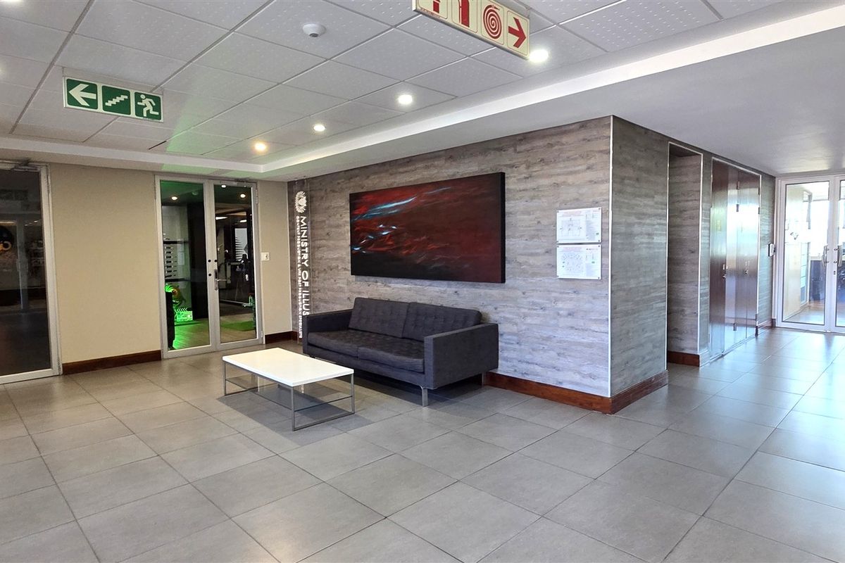 A modern office building entrance lobby featuring tiled flooring, a wood-look feature wall, recessed lighting, and multiple glass-panelled access doors.