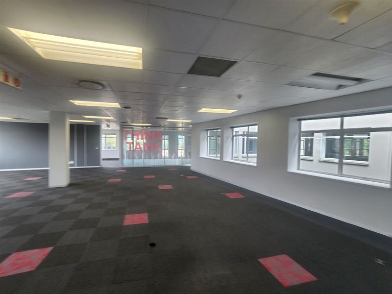 Spacious open-plan office area featuring suspended ceilings, recessed lighting, and carpeted flooring with large windows providing ample natural light.