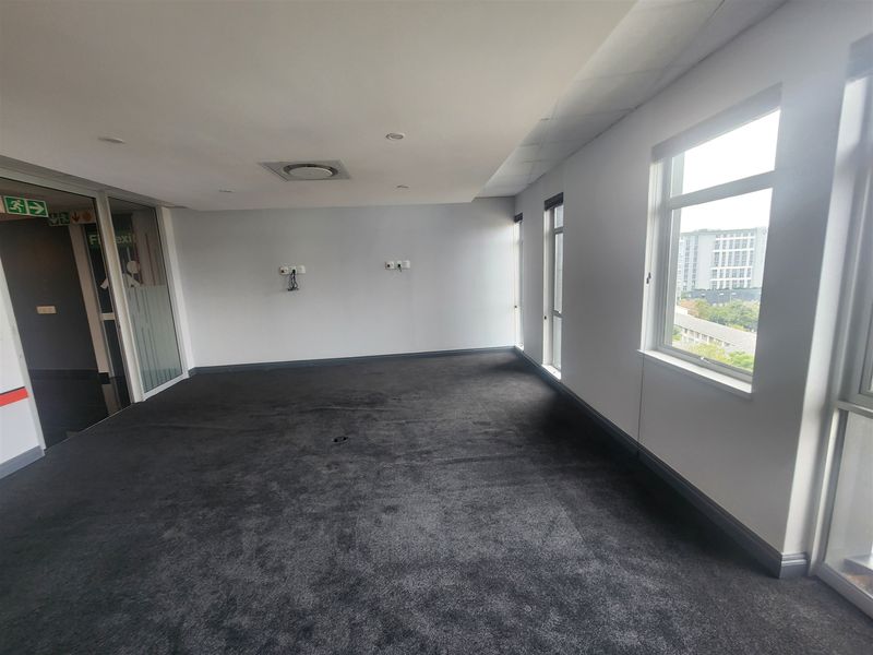 A vacant, open-plan office space featuring dark carpeting, large windows providing natural light, and integrated electrical and data connectivity points.