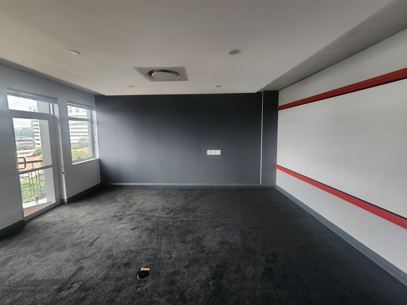 A vacant office space featuring dark carpeting, recessed ceiling lighting, and large windows providing natural light and exterior views.