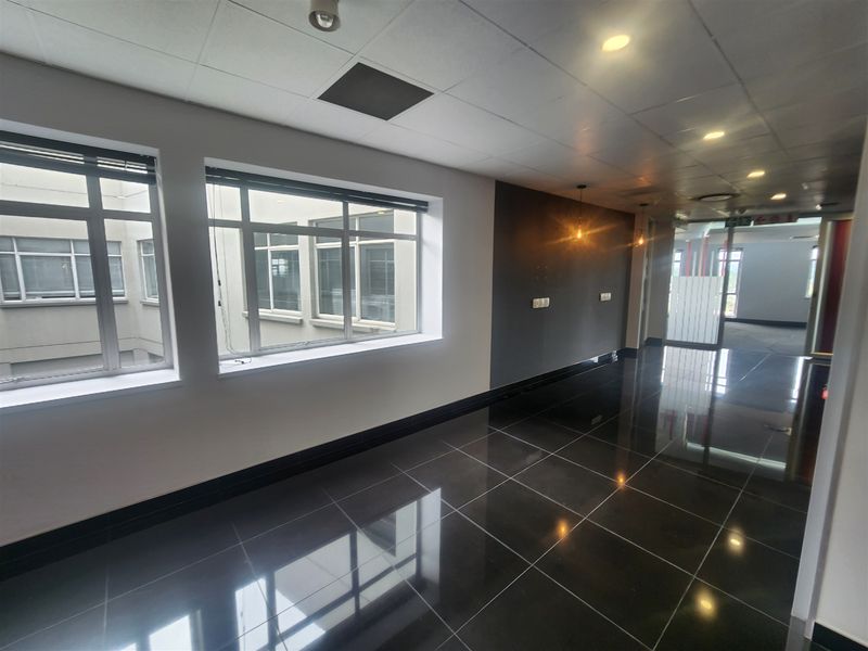 A bright, modern office space featuring polished dark tiled flooring, suspended ceilings with recessed lighting, and large windows providing natural light.