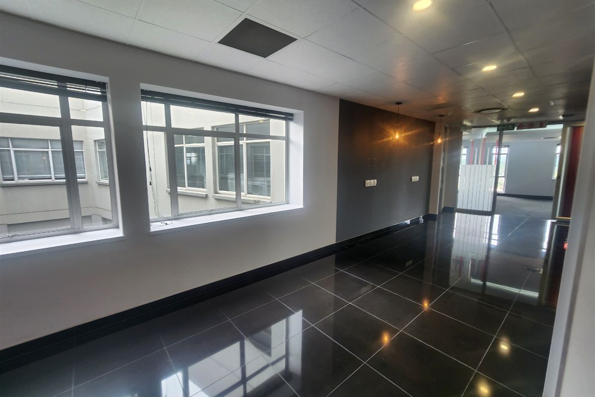 A bright, modern office space featuring polished dark tiled flooring, suspended ceilings with recessed lighting, and large windows providing natural light.