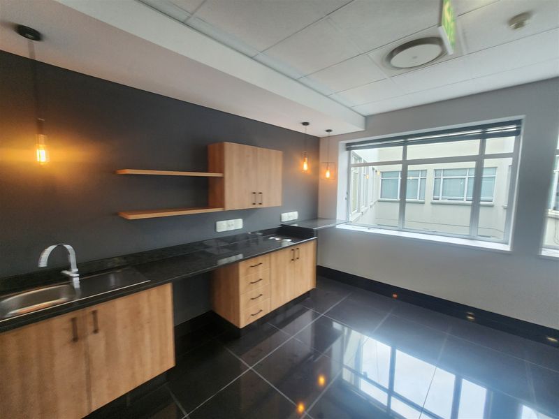 Modern office kitchenette featuring sleek wood-finish cabinetry, dark granite countertops, stainless steel sink, and polished tile flooring in a bright, professional workspace.