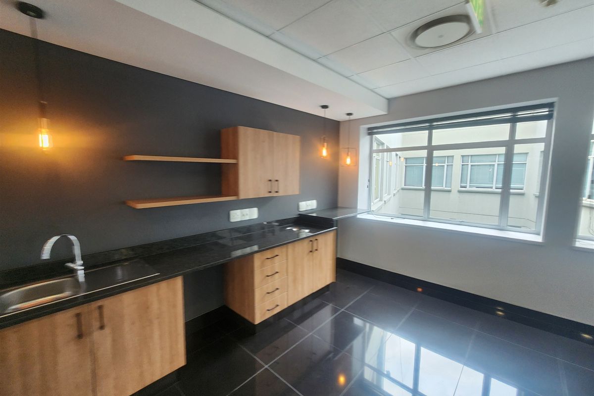 Modern office kitchenette featuring sleek wood-finish cabinetry, dark granite countertops, stainless steel sink, and polished tile flooring in a bright, professional workspace.