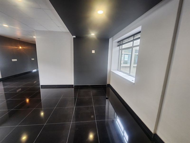 A modern, vacant office space featuring high-gloss tiled flooring, a suspended ceiling, and contemporary dark-toned accent walls with recessed lighting.