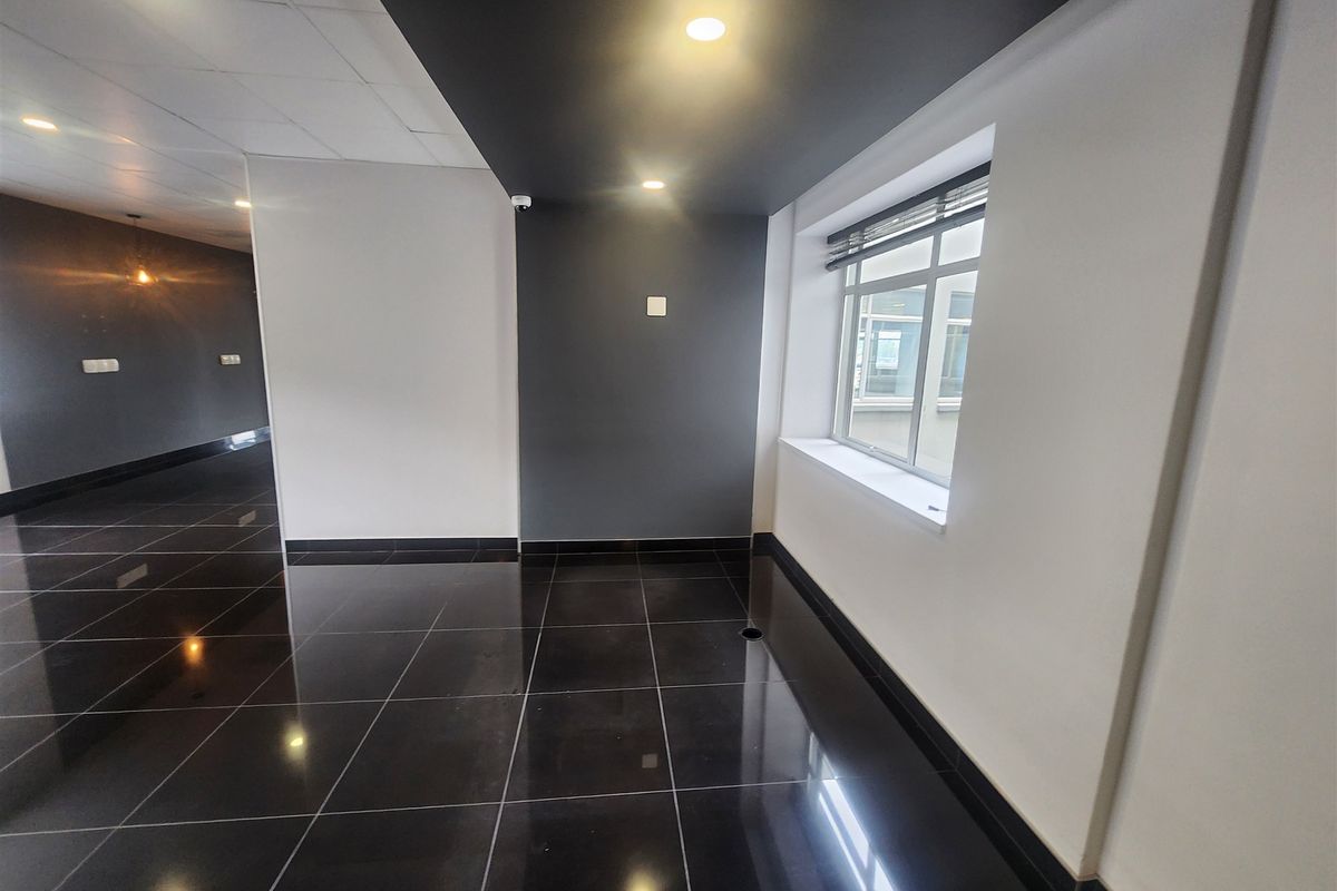 A modern, vacant office space featuring high-gloss tiled flooring, a suspended ceiling, and contemporary dark-toned accent walls with recessed lighting.