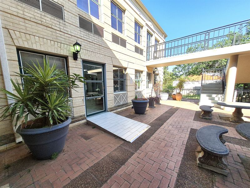 Rear exterior view of the office building featuring a paved courtyard, accessibility ramp, and an elevated walkway connecting building sections.