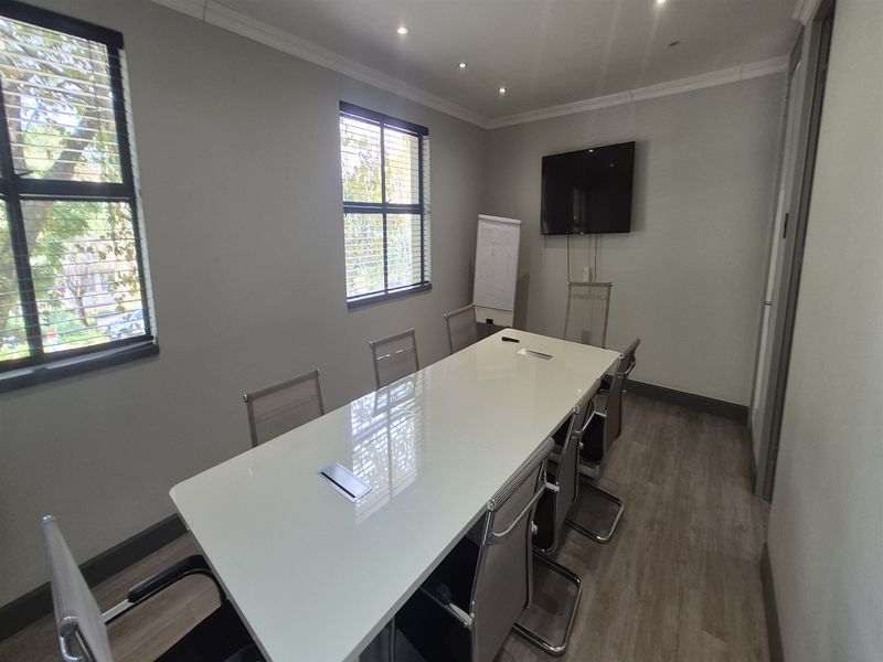 A well-maintained office meeting room featuring laminate flooring, recessed downlights, and large windows with venetian blinds.