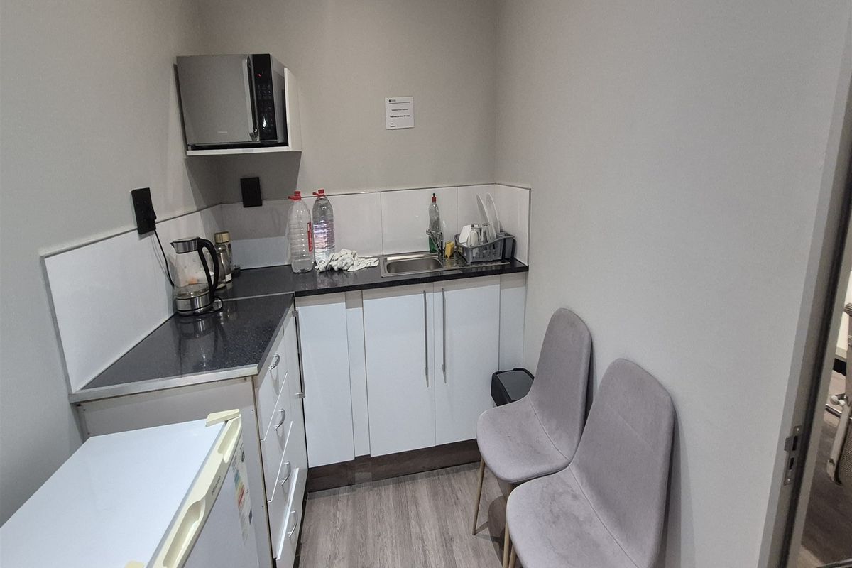 A compact office kitchenette featuring white cabinetry, dark laminate countertops, a stainless steel sink, and a dedicated shelf for a microwave.