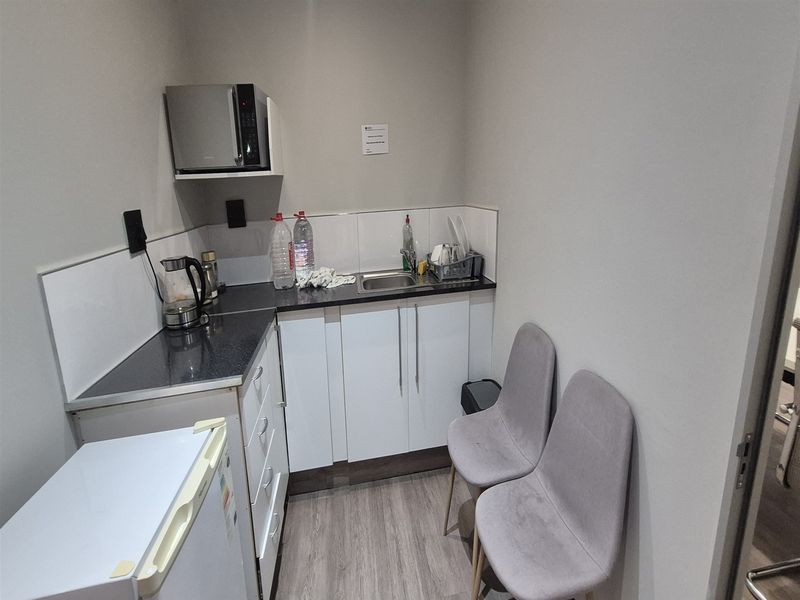 A compact office kitchenette featuring white cabinetry, dark laminate countertops, a stainless steel sink, and a dedicated shelf for a microwave.