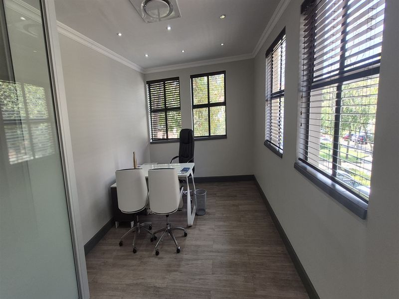 A bright and modern office space featuring laminate flooring, recessed lighting, and large windows with fitted venetian blinds.