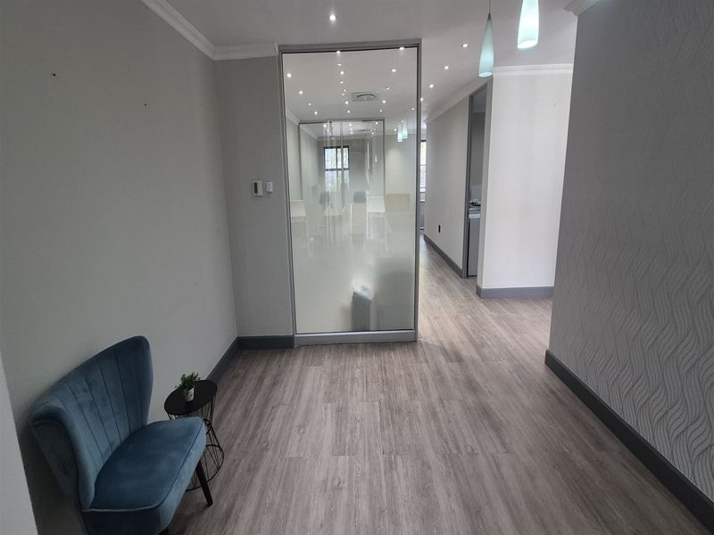 Modern office space featuring laminate flooring, recessed downlighting, and a contemporary glass partition creating a private workspace area.