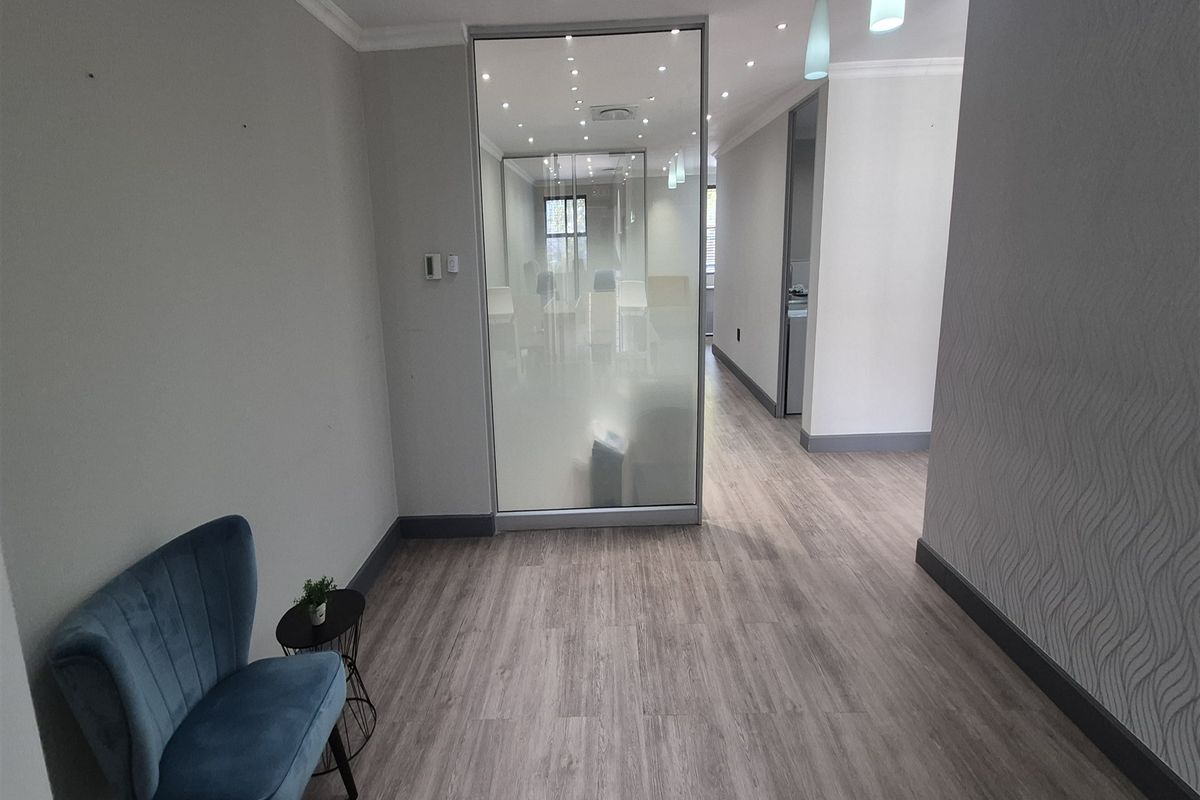 Modern office space featuring laminate flooring, recessed downlighting, and a contemporary glass partition creating a private workspace area.