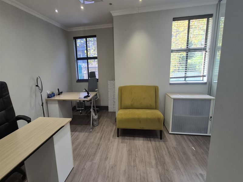 A well-lit office space featuring laminate flooring, recessed downlights, and large windows with venetian blinds, providing a professional and functional work environment.