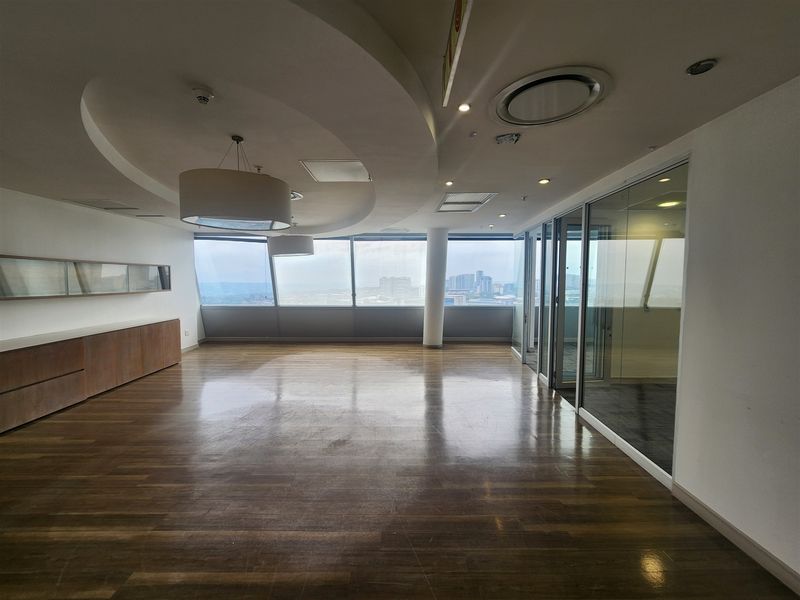 Spacious open-plan office area featuring hardwood flooring, floor-to-ceiling windows with city views, built-in cabinetry, and modern glass partition walls.