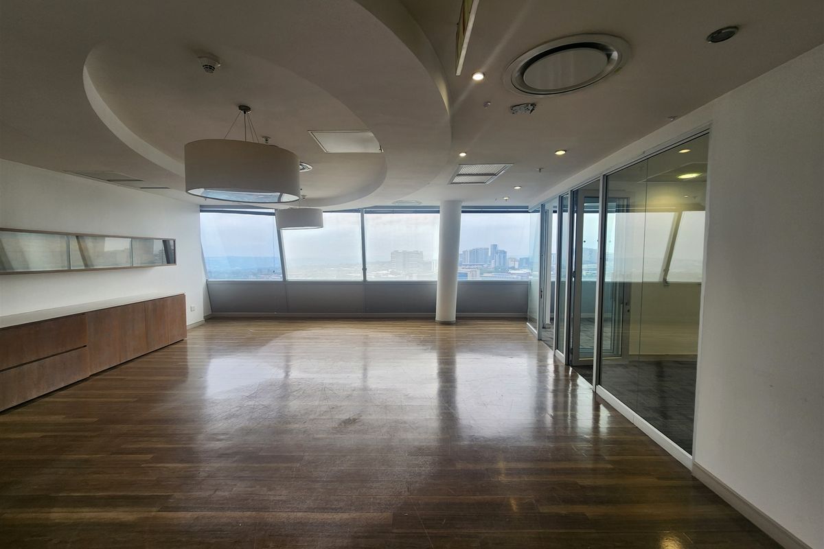 Spacious open-plan office area featuring hardwood flooring, floor-to-ceiling windows with city views, built-in cabinetry, and modern glass partition walls.