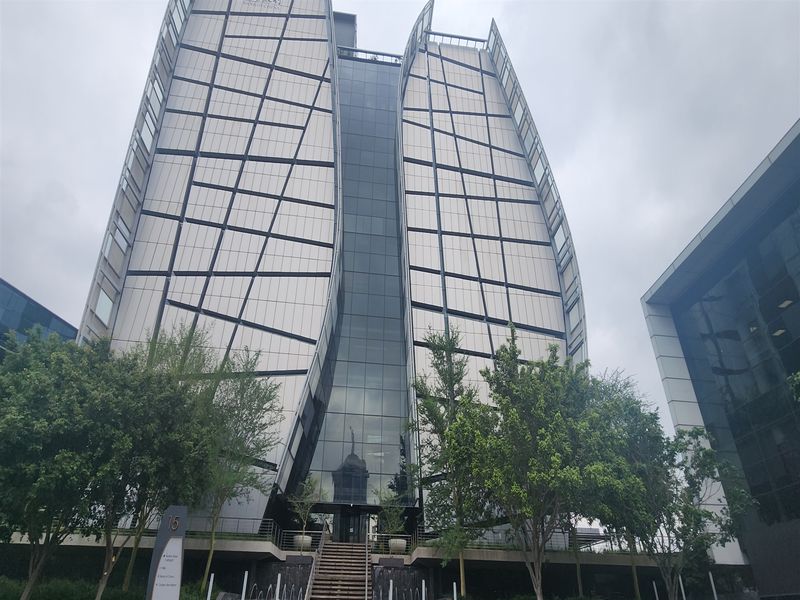 Modern commercial office building featuring a striking curved glass and metal panel facade with a landscaped entrance and water feature.