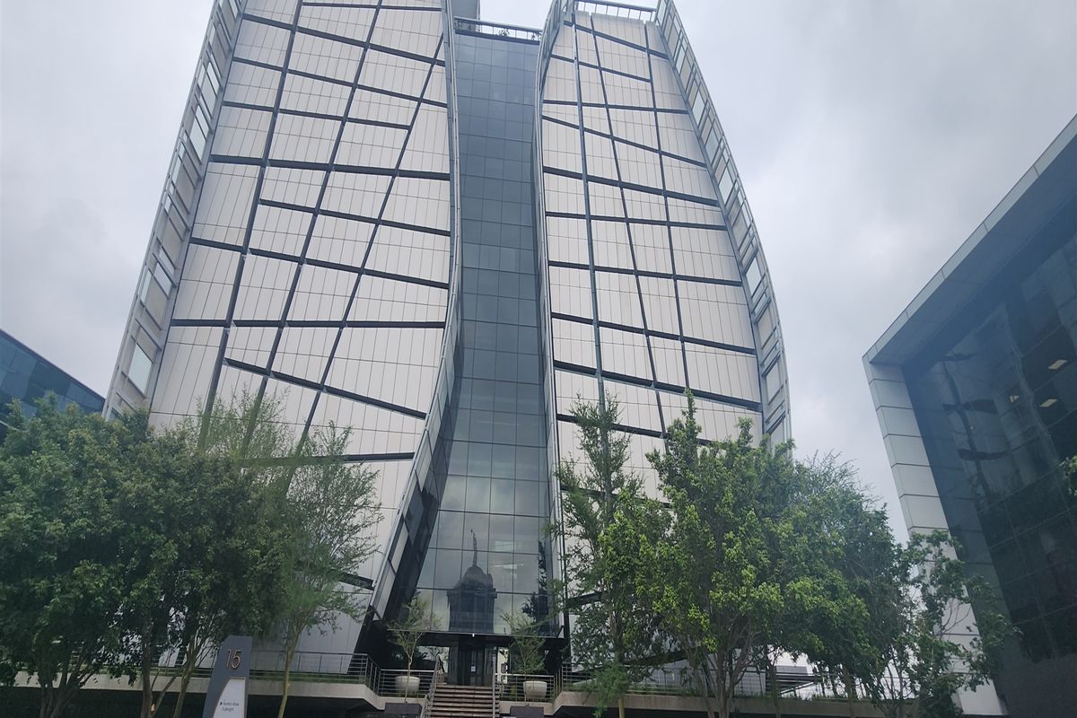 Modern commercial office building featuring a striking curved glass and metal panel facade with a landscaped entrance and water feature.