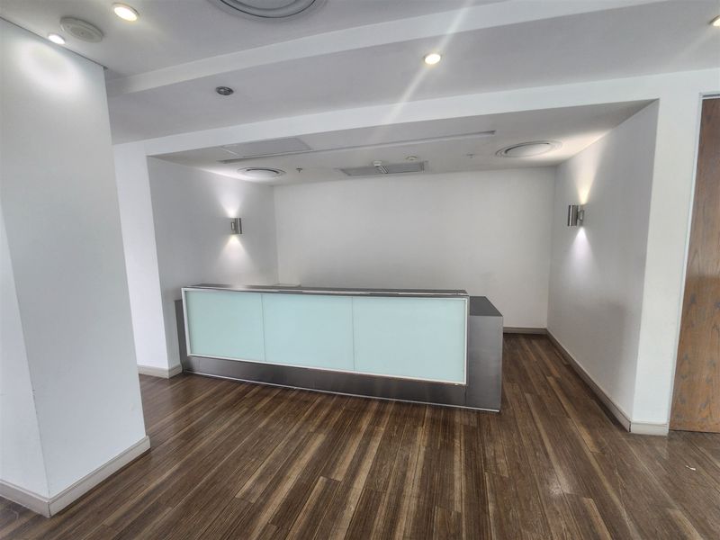 A professional office reception area featuring a modern built-in desk, recessed lighting, wall sconces, and durable laminate wood flooring.