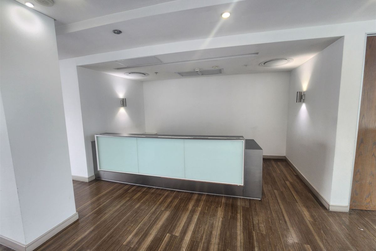 A professional office reception area featuring a modern built-in desk, recessed lighting, wall sconces, and durable laminate wood flooring.
