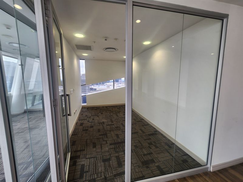 A modern, empty office space featuring glass partition walls, recessed lighting, and patterned carpet tiles, offering a clean and professional environment.